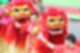 Performers in red costumes do a lion dance with vibrant red and gold lion heads. Background features decorative patterns. Energetic mood.