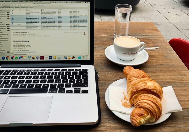Un laptop à côté d'une tasse de café et un croissant