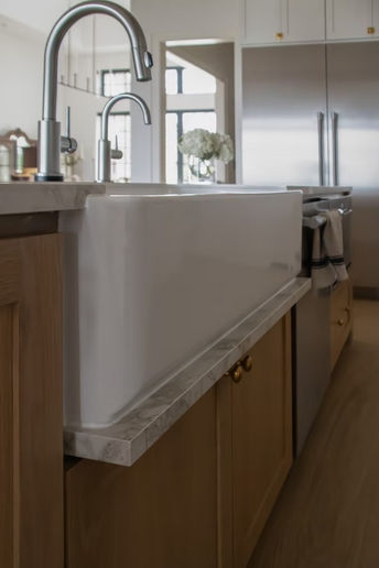 White farmhouse sink with modern faucet in a kitchen island.