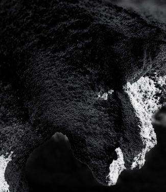 The Plague Doctor by Roee Baldinger (Cerno Argus). High-contrast dark fine art photography capturing a heavy, jagged rock silhouette resembling a masked plague doctor emerging from deep-crushed shadows. Part of the Psychosis of a Matter sub-series.