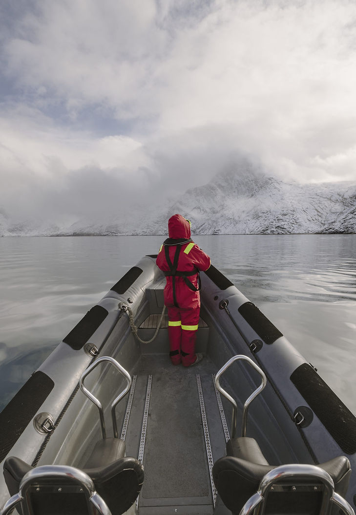 Person kayaking through icy Arctic waters surrounded by snow-covered mountains near Camp Kiattua, Greenland.