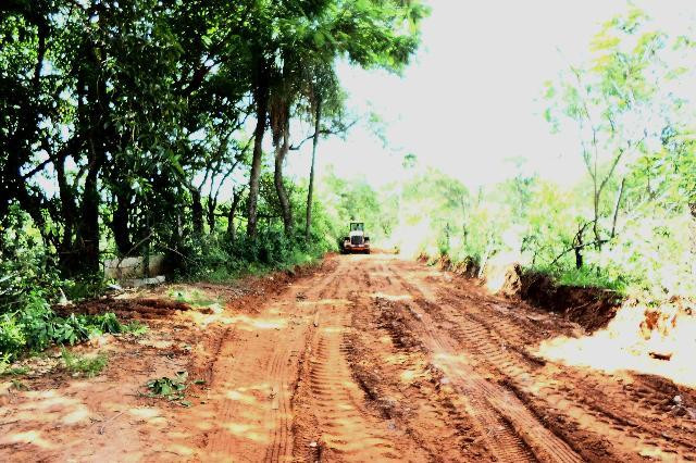 A foto mostra uma estrada de terra e um trator passando por ela.