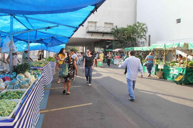 Pessoas andando nas feiras. Nos dois lados da rua tem barracas com alimentos expostos.