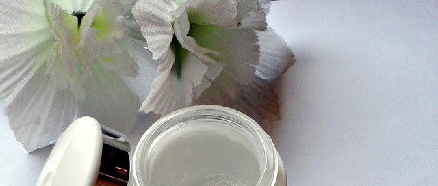 Canto esquerdo à cima uma flor falsa e abaixo no centro a metade de um pote redondo de algum cosmético.