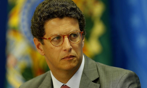 A imagem mostra o ministro do meio ambiente Ricardo Salles com uma cara que aparenta preocupação. O fundo está com o símbolo da República desfocado.