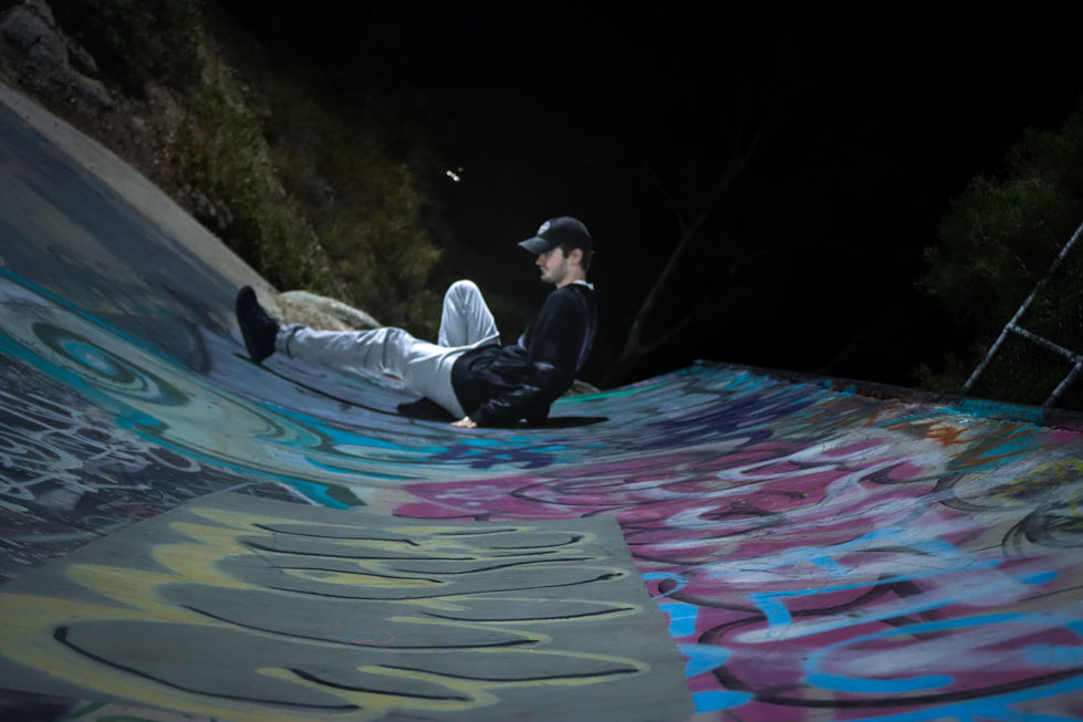 Man at night in skatepark with graffiti sitting on ramp