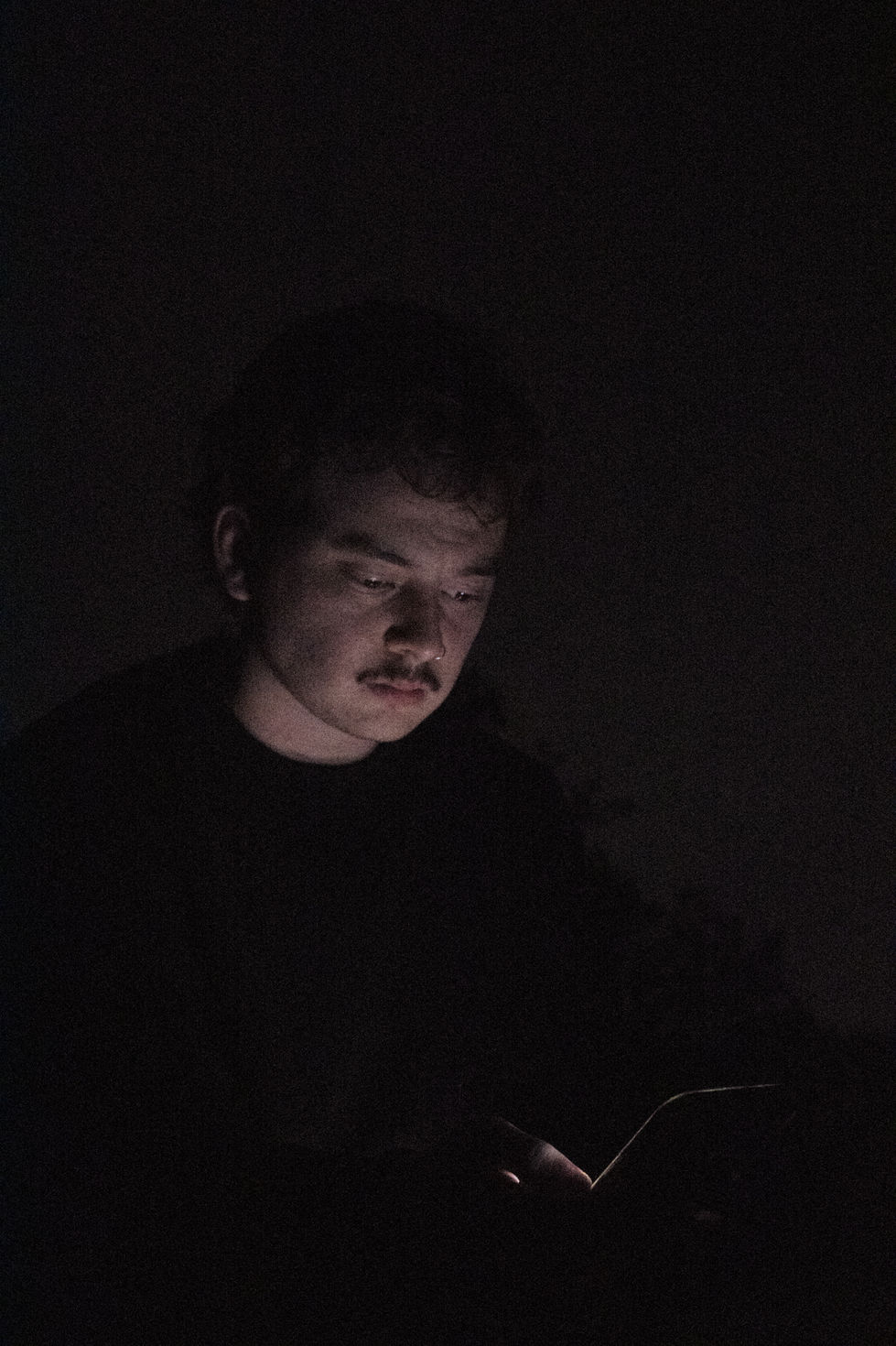 Man clothes blending into background, staring at phone, phone barely lighting up face, lightness 2/10