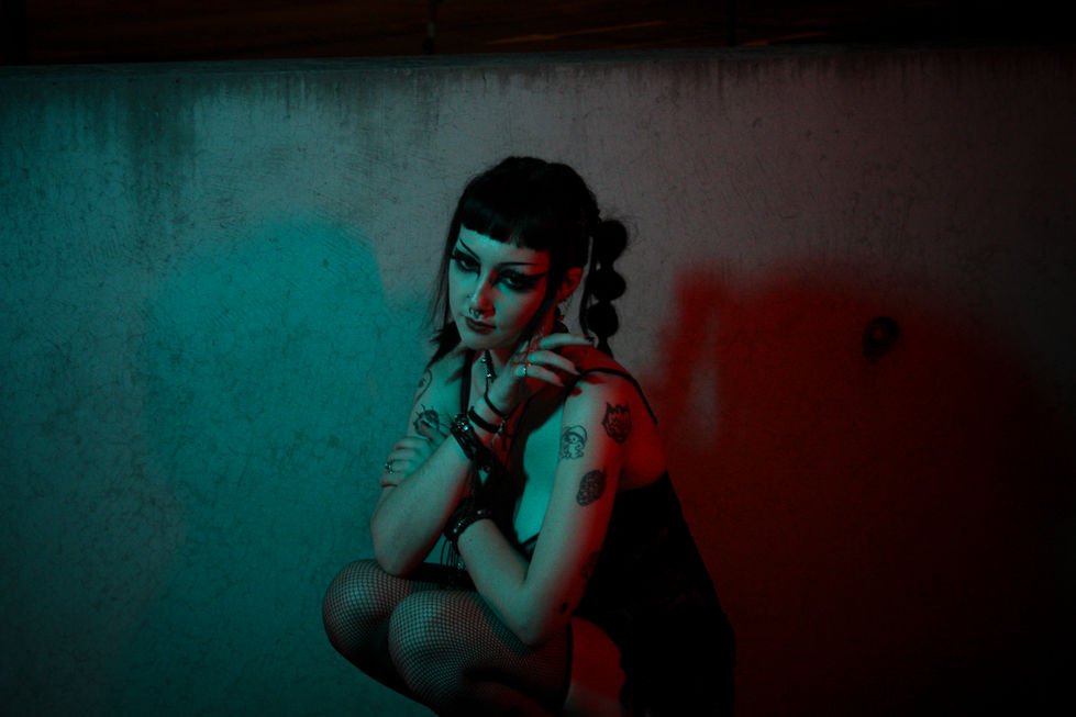 Neon lights at night shining on model posing in front of blank wall crouched down closed off