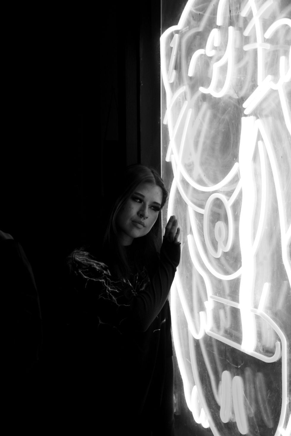 Late night photo in Perth city of woman standing next to neon sign staring into camera