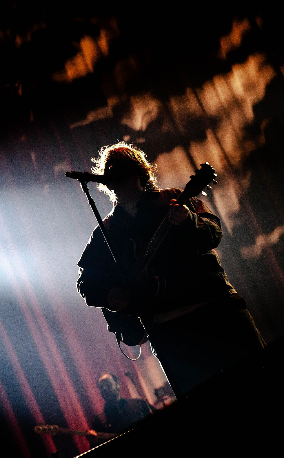 A man (Lewis Capaldi) playing guitar in a silhoutte with orange and red lights behind him