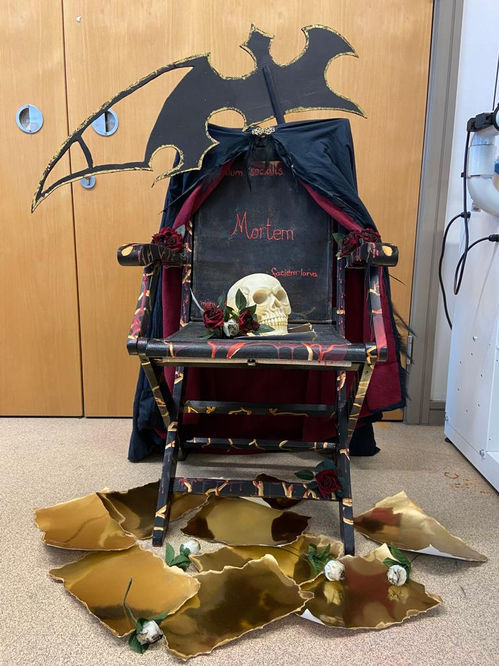a black chair with a skull on the seat, a cloak draped over the back and a scythe standing behind it