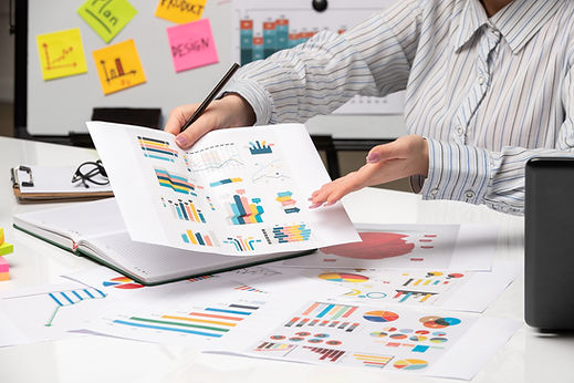 person in a striped shirt explains business charts and graphs to someone off-camera in an office setting.