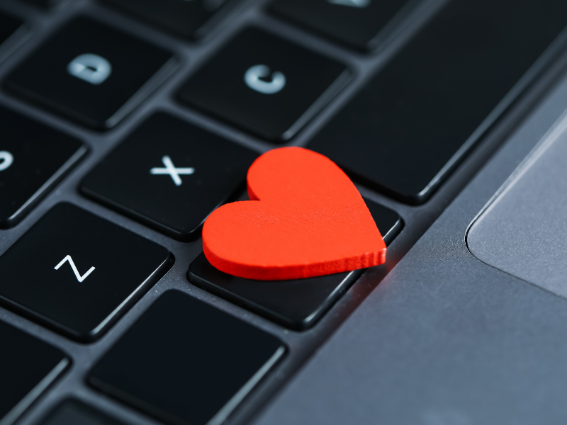 A heart shaped piece of wood sitting on laptop keys.