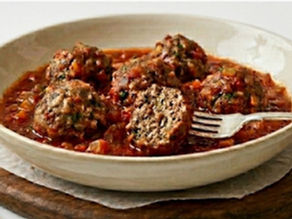 Juicy meatballs in pasta sauce served in a white bowl.