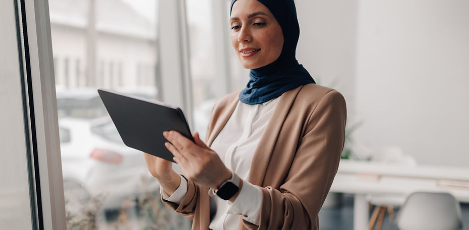 Muslim businesswoman wearing a hijab and a beige suit smiles while using a digital tablet