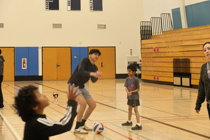 Children and a coach practicing volleyball in a gym.