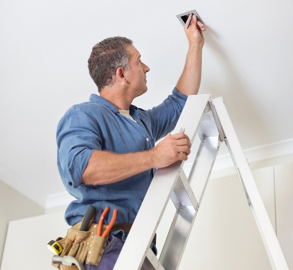 A man diligently fixing a ceiling fan, ensuring optimal functionality and comfort in the room.