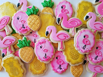 Decorative flamingo-shaped and pineapple cookies with detailed pink and gold icing, perfect for themed parties or tropical celebrations.