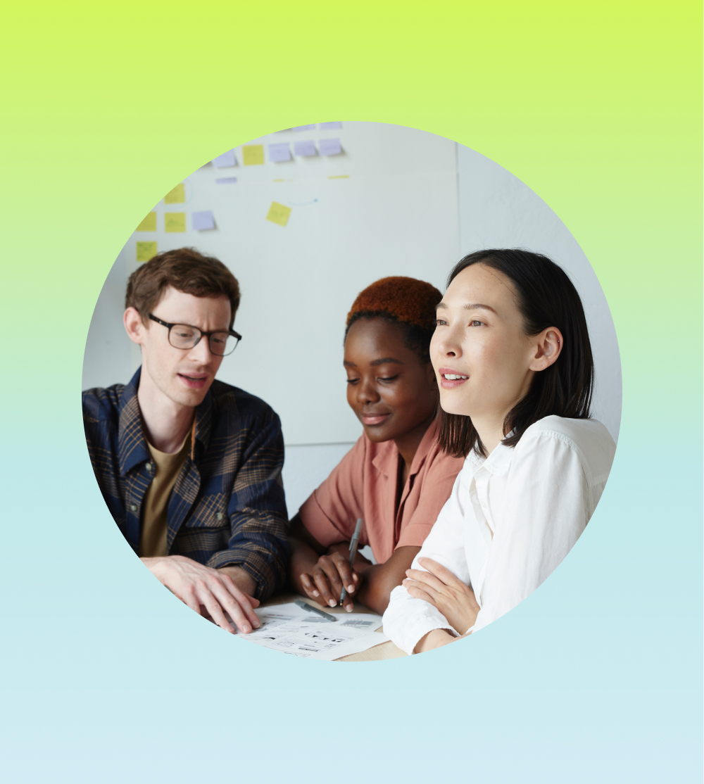 A man and two women are sitting at a desk reviewing documents, this image is circular surrounded by a blue and yellow square. 