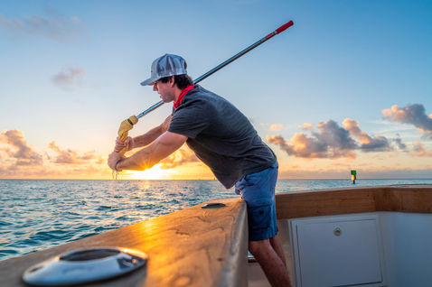 Man wringing a mop from a boat at sunrise.