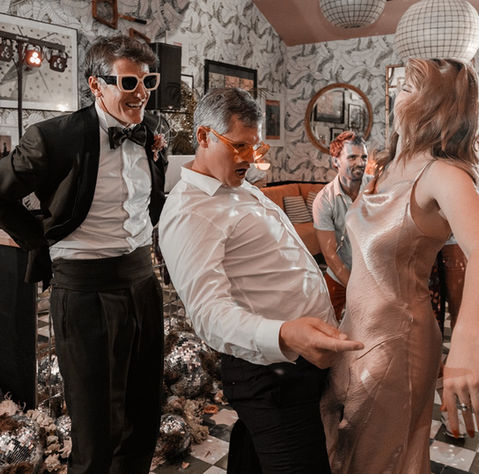 Groom and guest in sunglasses dancing energetically at a wedding reception.