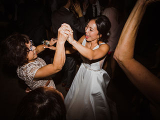 The bride, in her elegant white gown, dances with an older female guest in a moment of joy and celebration, surrounded by other guests enjoying the festivity.