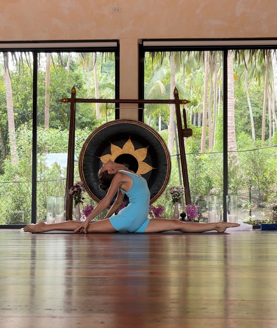 Woman performing a split with a gong behind her. Private Yoga Session with Kira. Heart Of Santosha