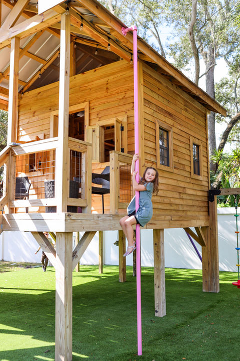 Young girl climbs a pink pole on a wooden playhouse, Firefly Forts.