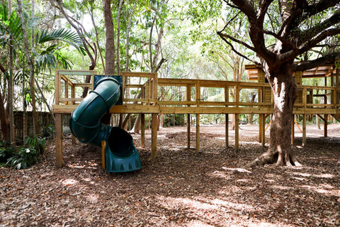 Elevated green slide connected to custom wood play structure with wraparound deck in South Florida.