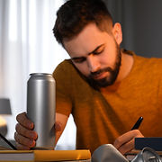 Man working at a desk holding an energy drink. 