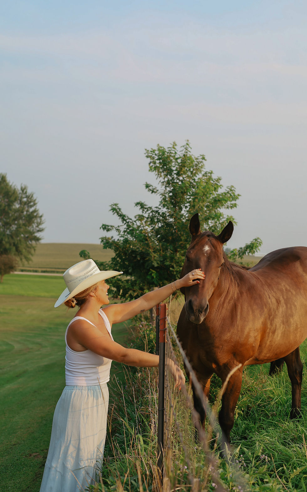 Woman wearing a custom hat standing beside a horse at an outdoor event
