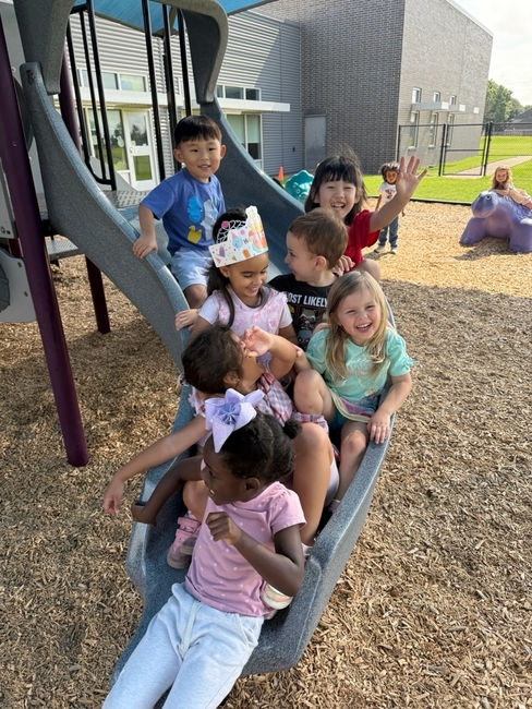 Smiling preschool children sitting together on a playground slide at CrossRoad Christian School in Katy, TX, enjoying outdoor