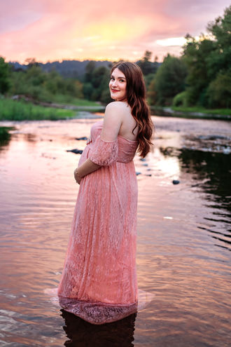 Maternity Photograph - a pregnant woman in a pink dress stands in shallow waters at sunset.