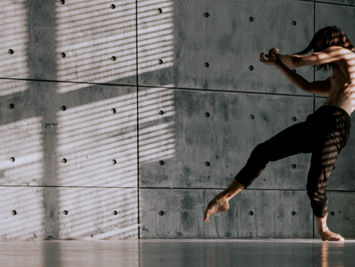 a shirtless man dacing alone next to a concrete wall