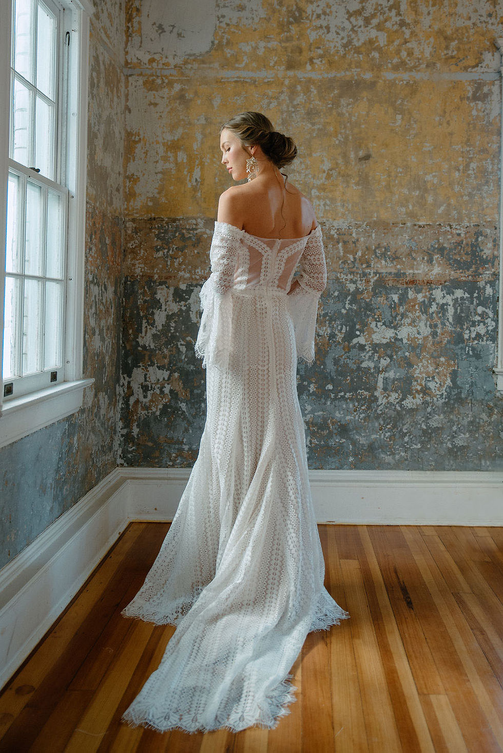 A back view of a bride wearing a bohemian lace wedding dress with a sheer back and long train.