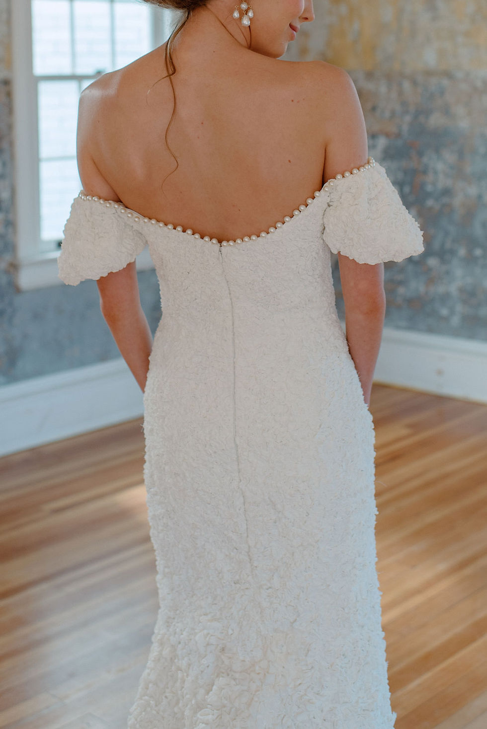 Thumbnail: Close up of the back details on an off the shoulder textured crepe wedding dress with a pearl neckline
