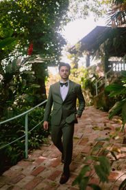 Groom walking along the brick pathway at Hacienda Siesta Alegre in a green suit