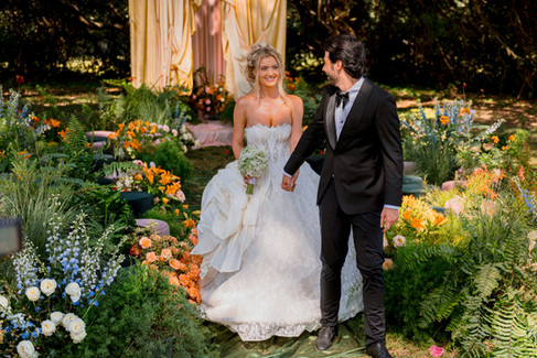 bride wearing a lace ball gown with a small white bouquet and groom wearing a black tuxedo in the wedding ceremony area