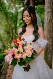 Bride smiling outdoors holding a vibrant tropical bouquet at Hacienda Siesta Alegre
