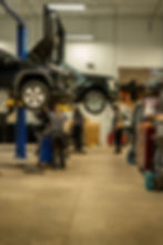Black Toyota Rav 4 with Ford f-150 with a female individual under car and two men under black truck one holding the front bumper with shop as background