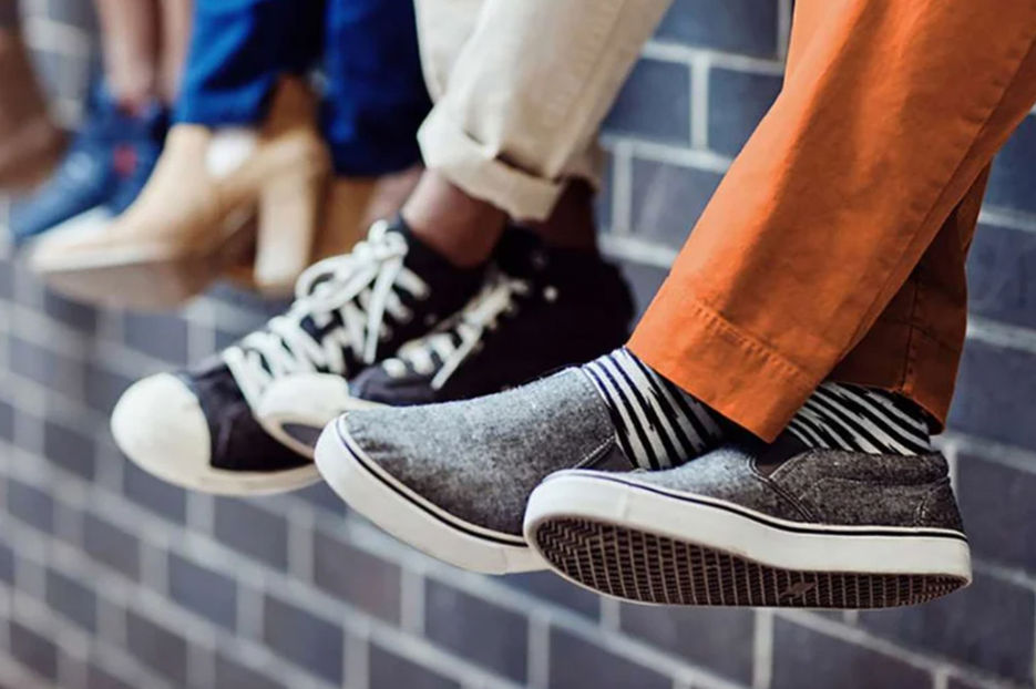 A line of people sitting on a wall with a focus on their shoes