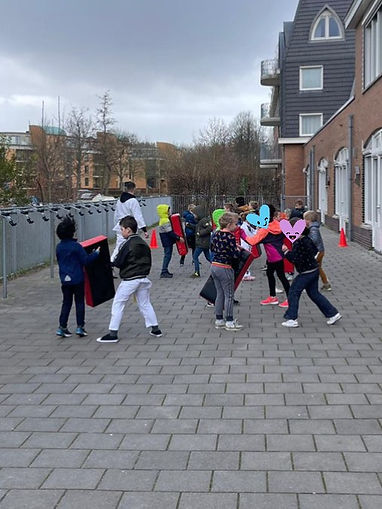 Kinderen oefenen stoot- en traptechnieken op schopkussens tijdens de les