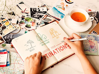 table remplie de photo avec un cahier ouvert sur lequel une personne écrit "choisi ta destination"
