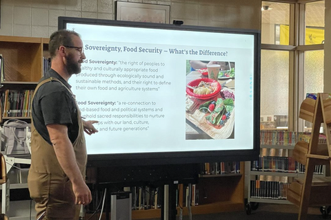 Teacher presenting in front of a smart board, discussing Problem-Based Learning and food security solutions to educators for classroom application.