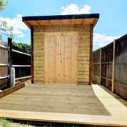 Modern wooden shed with flat roof and new deck in fenced yard.