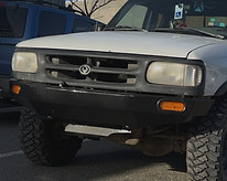 White truck with black bumper and large tires, parked outdoors