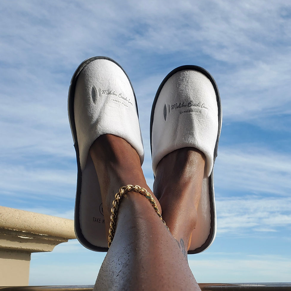Relaxed guest feet wearing Malibu Beach Inn slippers against a clear blue sky, symbolizing leisure and comfort at a luxury beachfront hotel