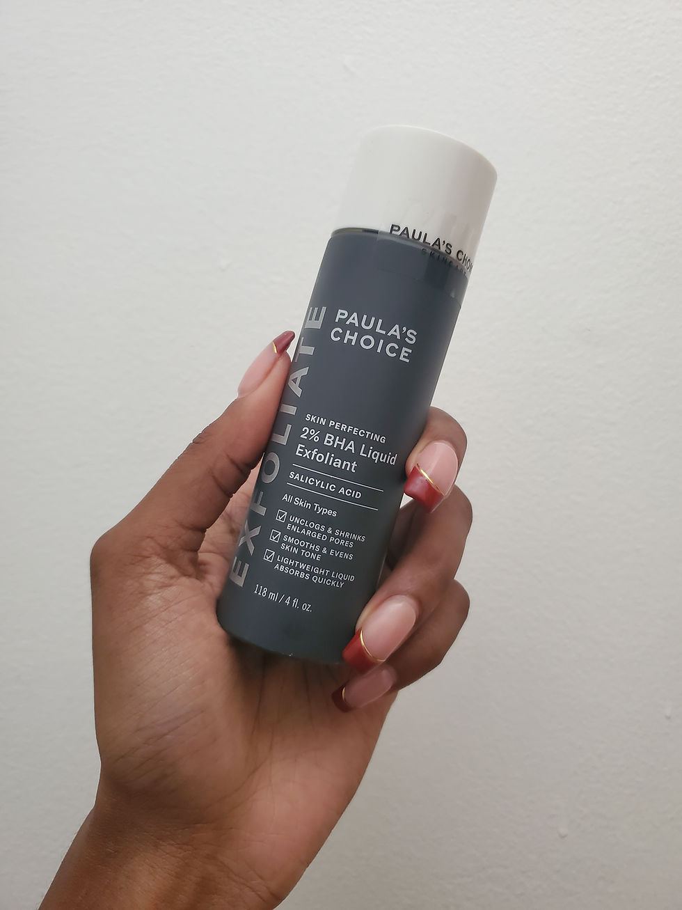 Paula's Choice Skin Perfecting Liquid: A cylindrical bottle with a navy-blue body and a white cap. The front label highlights it as "Paula's Choice Skin Perfecting 2% BHA Liquid Exfoliant". Key features mentioned on the bottle include its suitability for all skin types and its lightweight formula that absorbs quickly. The product contains salicylic acid and is 4 fl. oz. or 118 ml in volume.