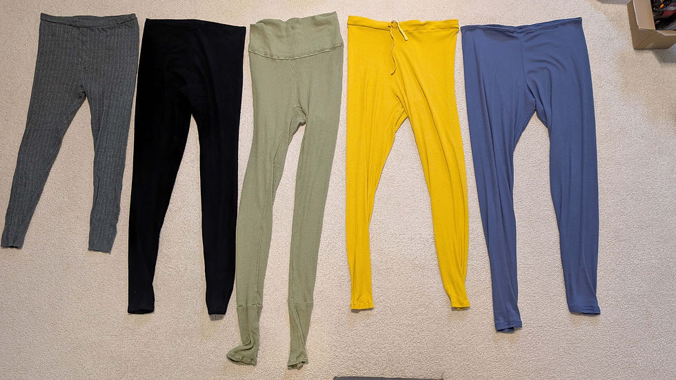 Five pairs of leggings in gray, black, olive, yellow, and blue are laid out on a beige carpet. A cardboard box is partially visible.