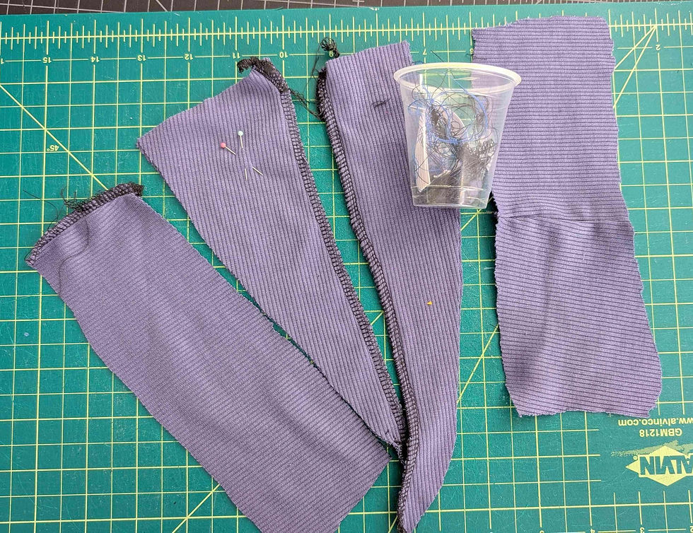 Purple fabric strips with serrated edges, sewing pins, and tangled threads in a clear cup on a green cutting mat with yellow grid lines.
